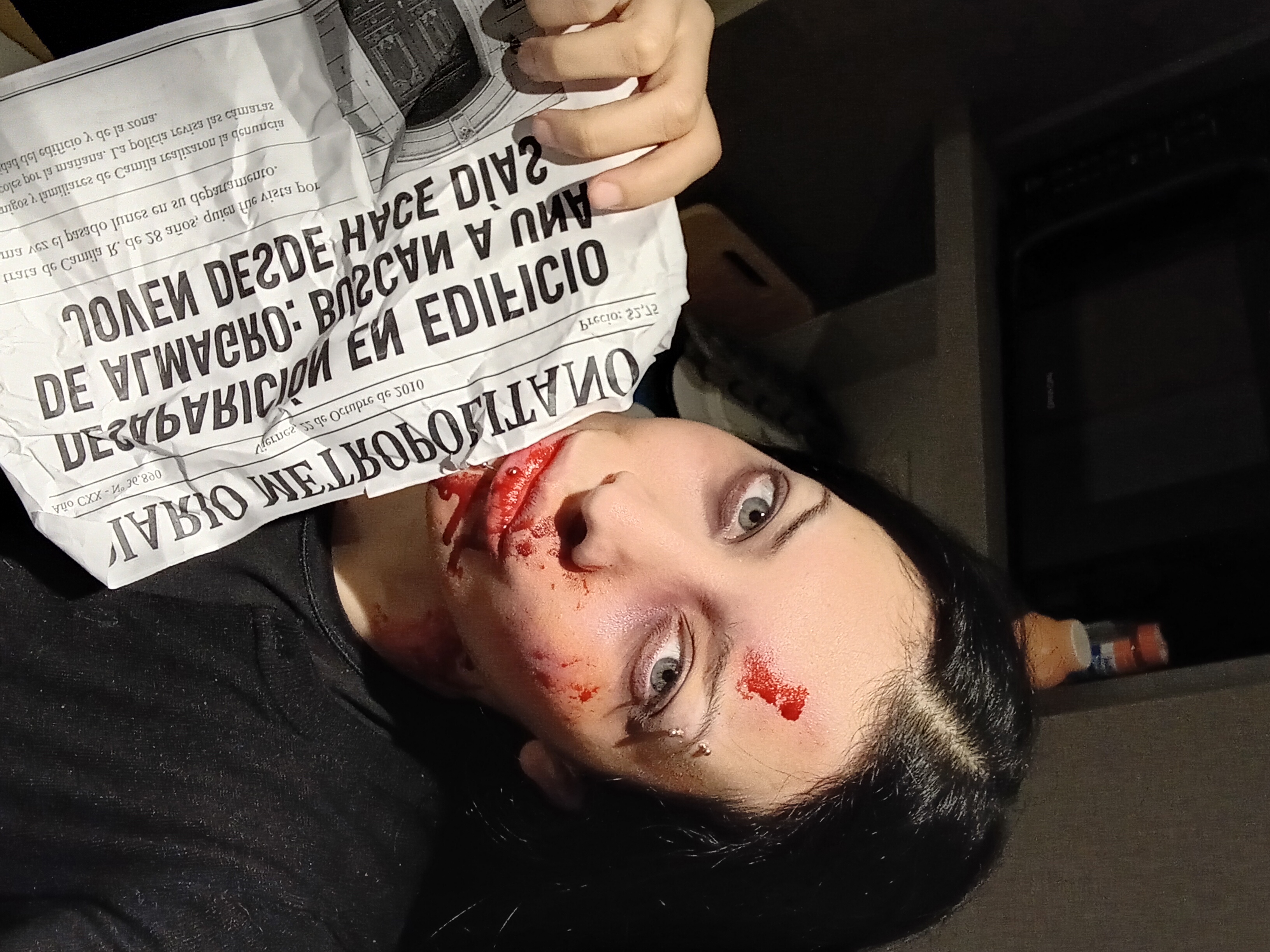 Zoe with horror SFX gore makeup holding a newspaper, fake blood on her face
